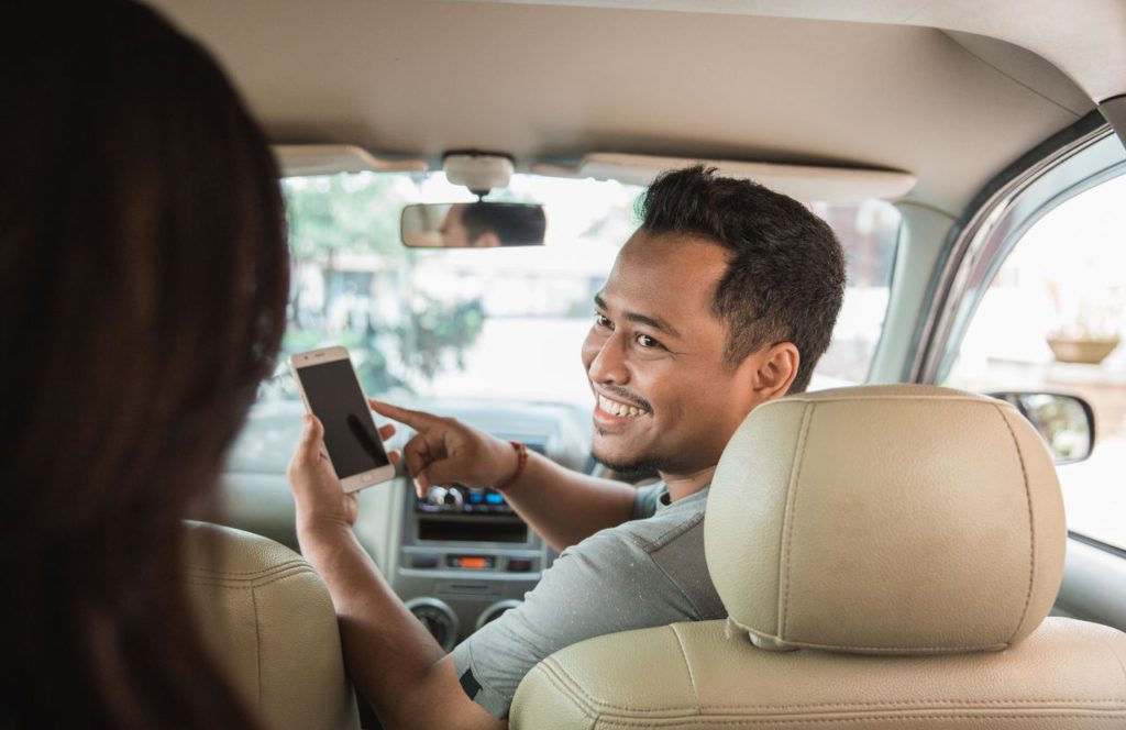 man in front passenger seat hold phone and looking at rear passenger and explain how to track mileage