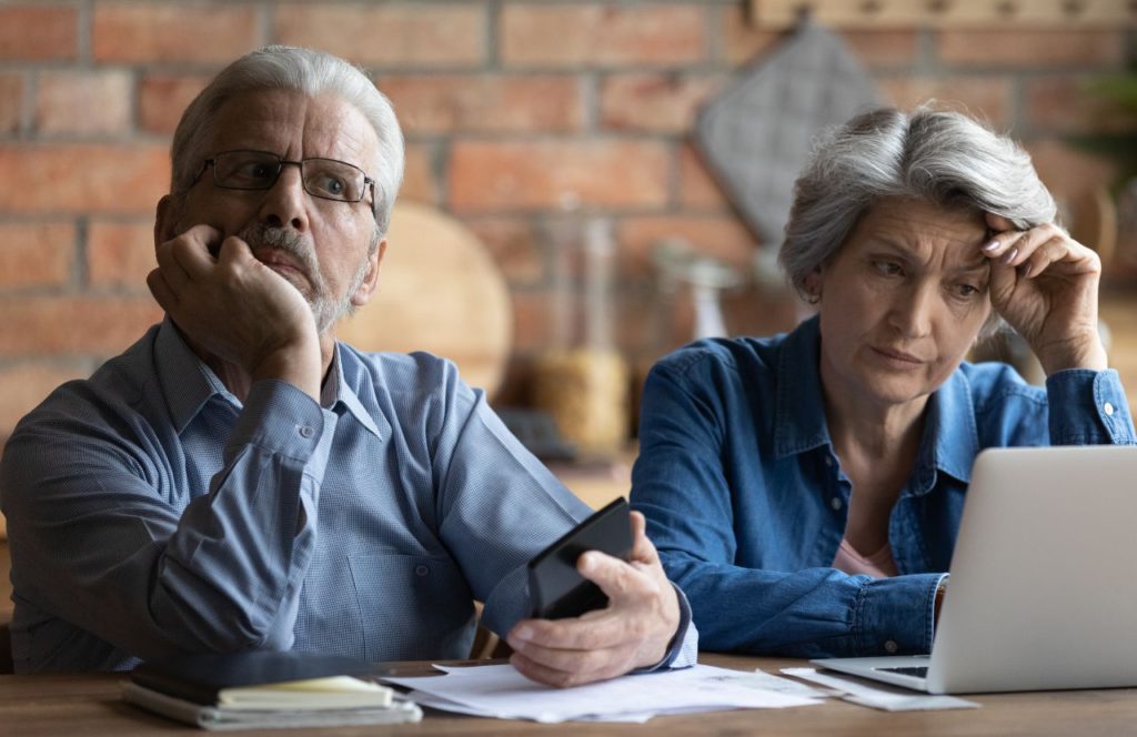 older frustrated couple man holding calculator looking at information on laptop on tax evasion vs tax fraud