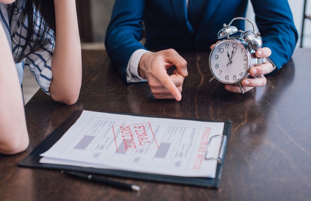 two people at a desk with man holding a clock and final notice for tax bill on a clipboard as taxpayer learn about what is tax resolution and when the payment is due