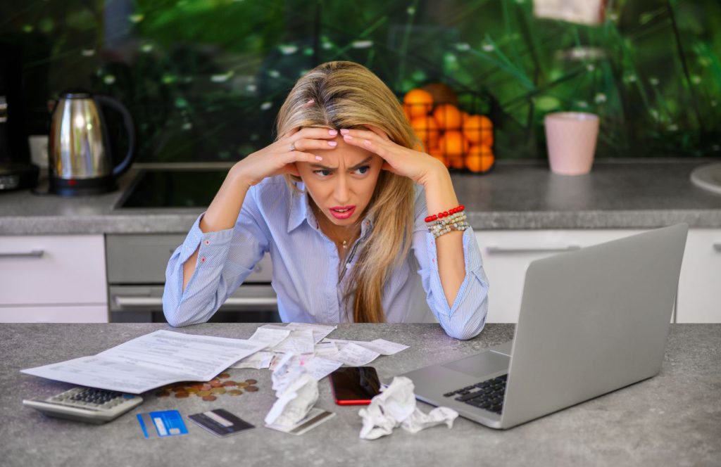 woman frustrated and stressed looking at her laptop, paperwork, credit cards, and bills needing tax resolution