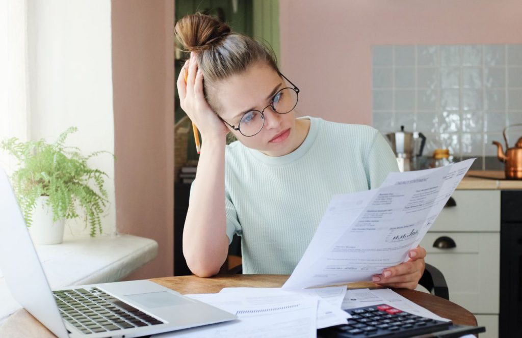 woman holding a pencil wearing glasses looking over a document at her desk looking confused on tax evasion vs tax fraud