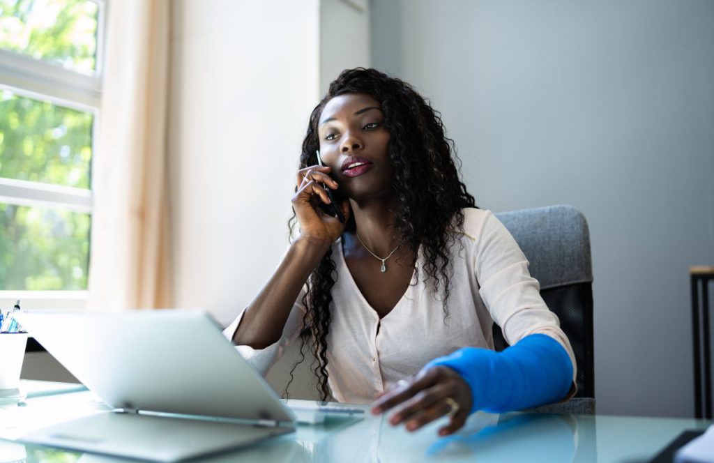 black woman sitting on the phone finding out is workers comp taxable with cast on left arm