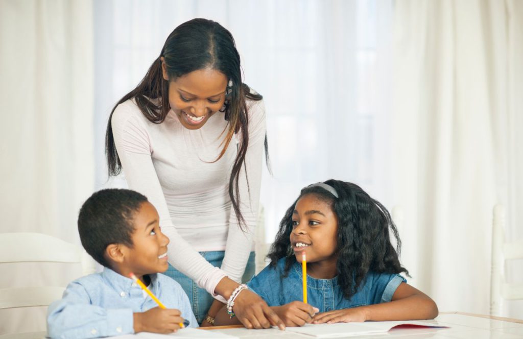 black woman smiling helping boy and girl do school work