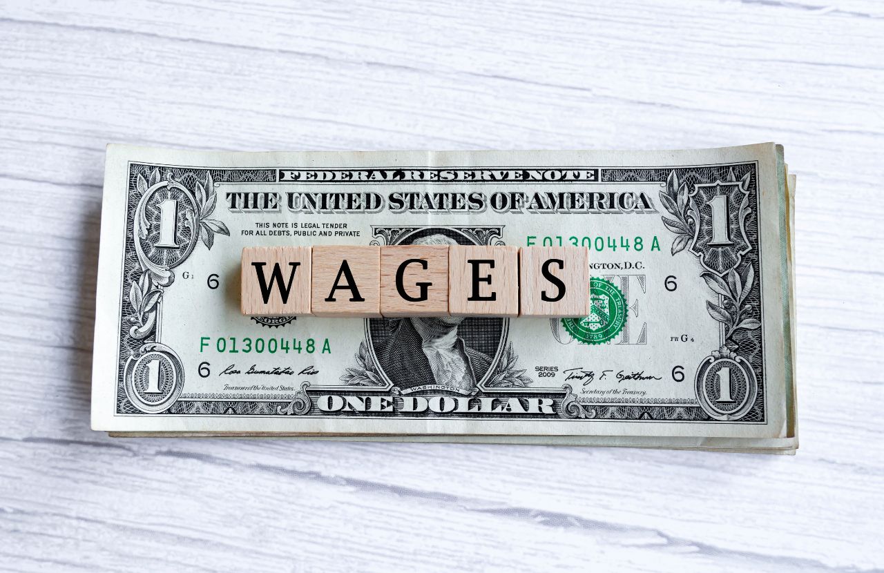 A visual representation of wages vs income on a block on a stack of dollars